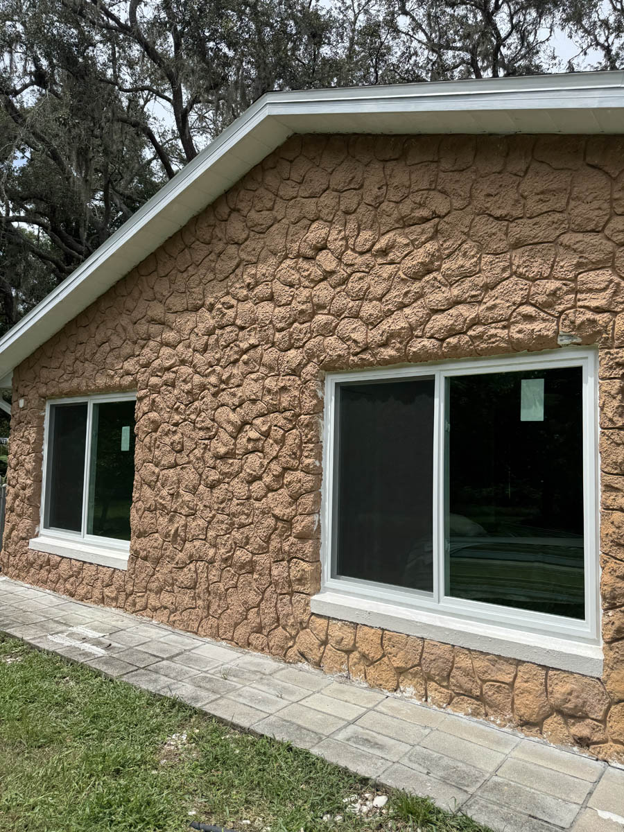 replace home windows Exterior view of a home with fresh window replacements, featuring two new white-framed sliding windows installed in a textured stone-finish wall.