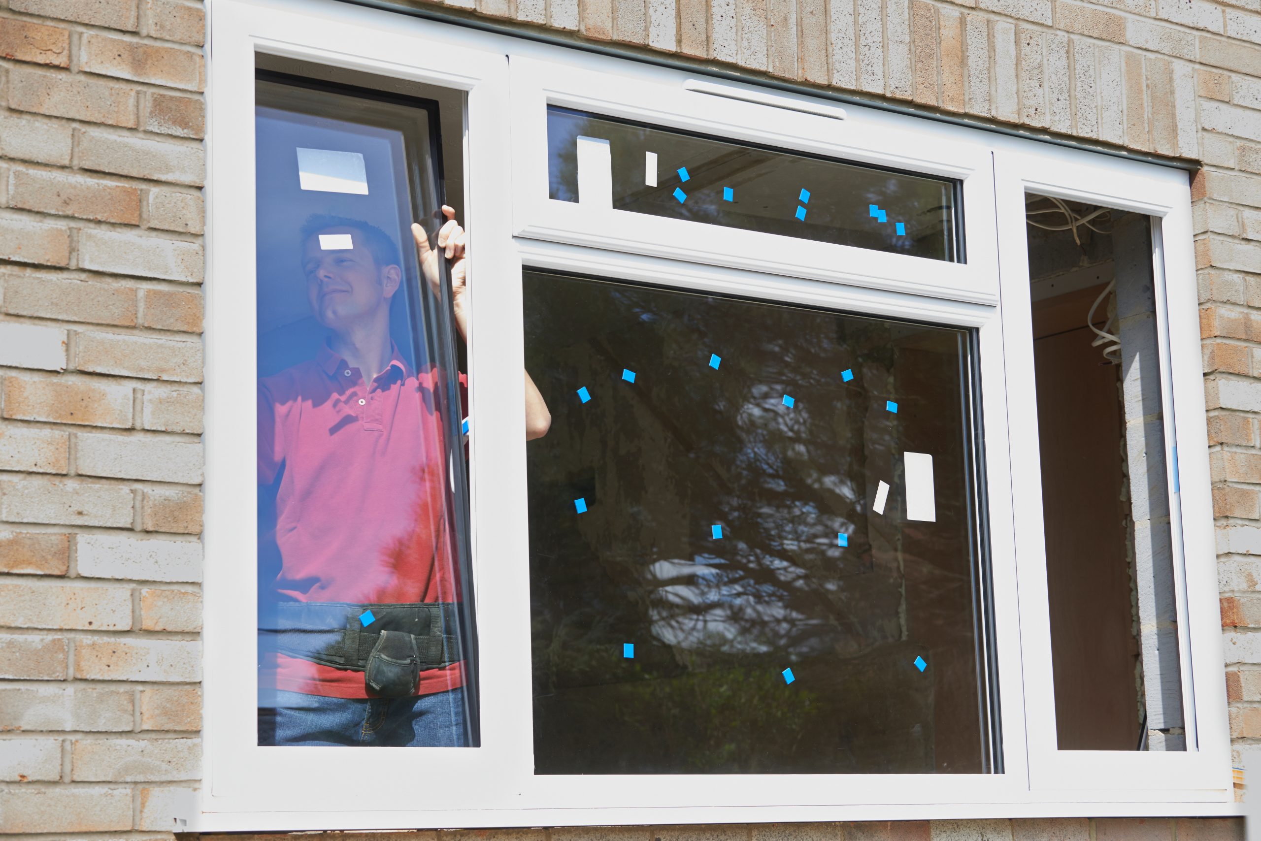 Construction Worker Installing New Windows In House Window installer fitting high performance white windows into the brick exterior of a home.